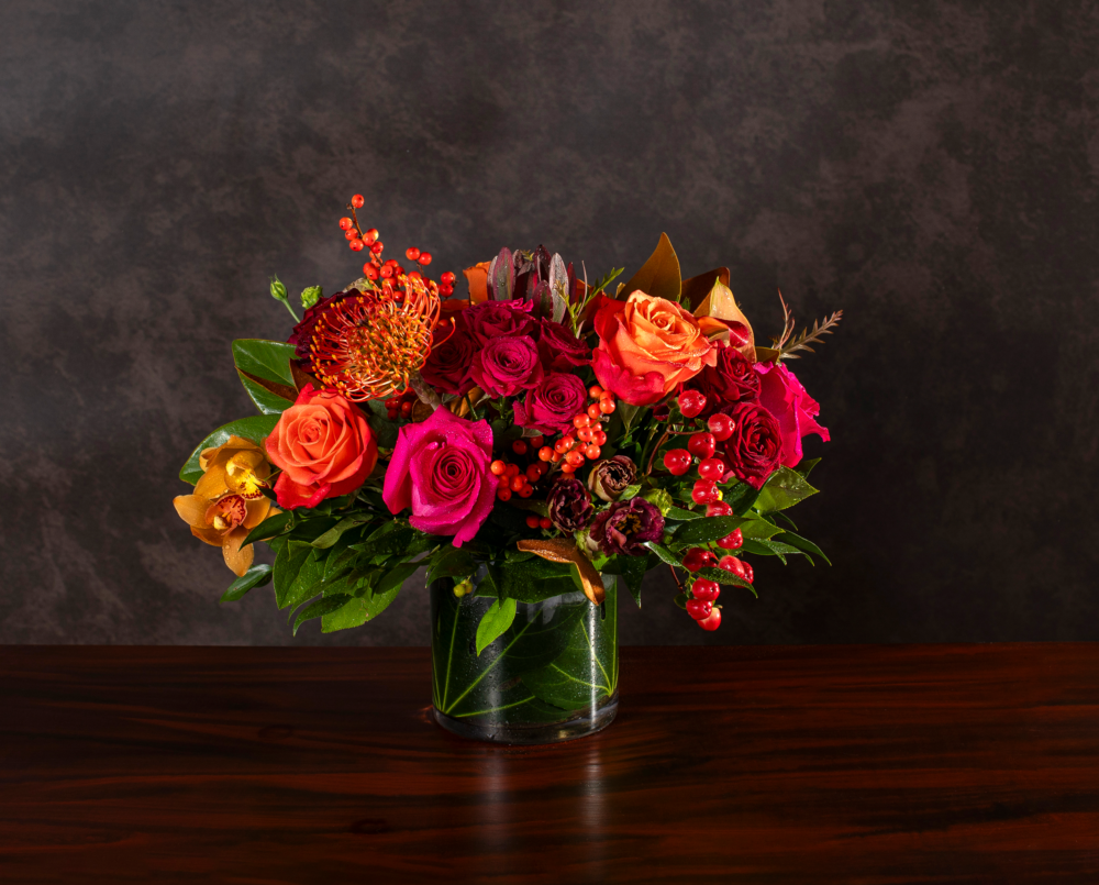 Della is a hot pink and orange flower arrangement in a glass cylinder vase with a leaf wrap.