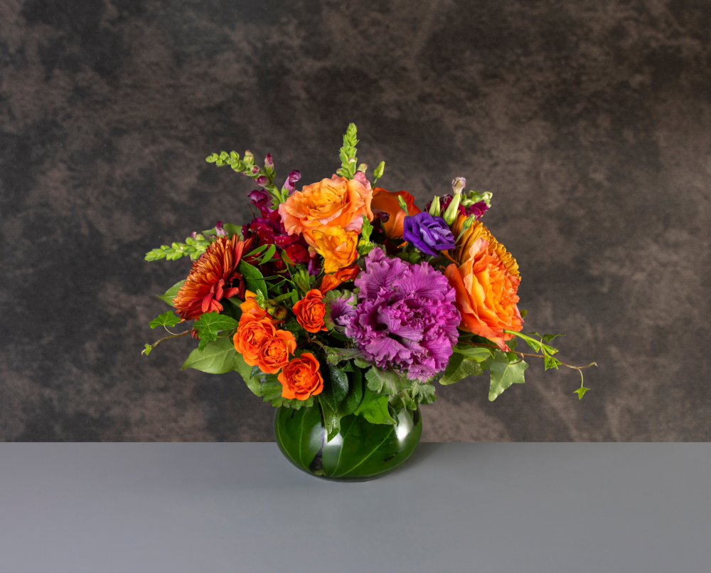 Jewel is a bright autumn flower arrangement in oranges and purples in a glass posey vase.