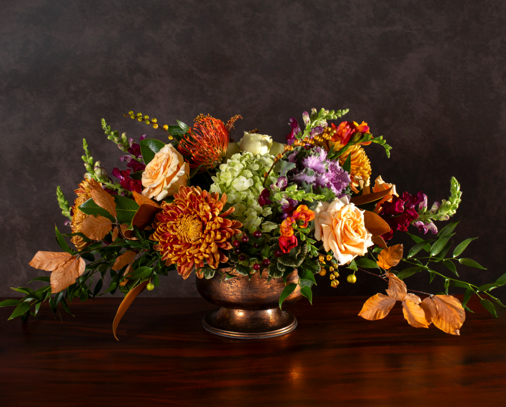 A deep orange, peach, purple, green, seasonal flower arrangement in a copper pedestal vase, delivered, thanksgiving